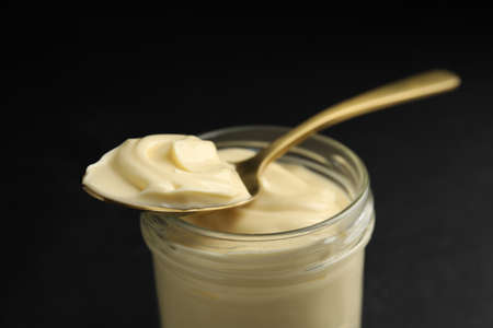 Jar of delicious mayonnaise and spoon on black table, closeupの写真素材