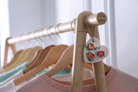 Beautiful heart shaped scented wax sachet and clothes hanging on wooden rack indoors, closeupの写真素材