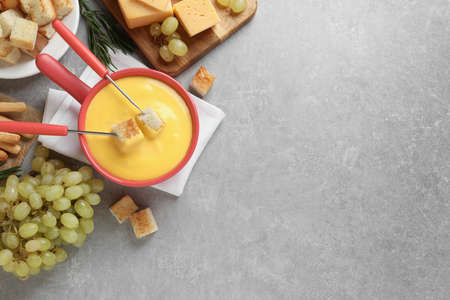 Flat lay composition with pot of tasty cheese fondue on gray table. Space for textの写真素材