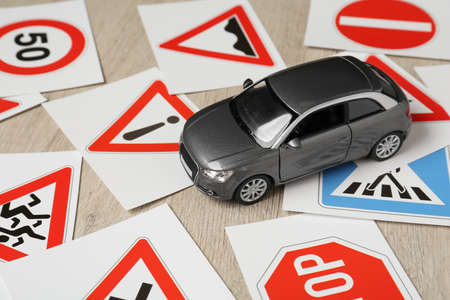 Cards with different road signs and toy car on wooden table. driving school
