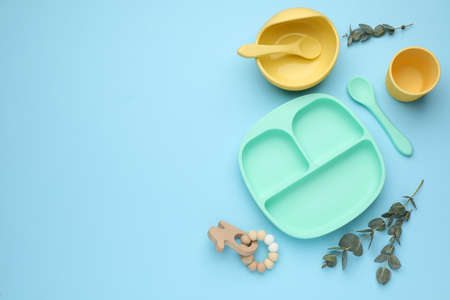Set of plastic dishware and wooden toy on light blue background, flat lay with space for text. Serving baby foodの写真素材