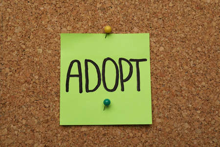 Note with word ADOPT pinned to cork boardの写真素材