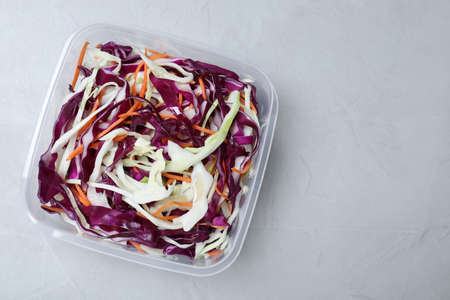Fresh cabbage salad with shredded carrot in plastic container on light table, top view. Space for textの写真素材