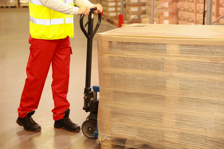 Worker moving wrapped wooden pallets with manual forklift in warehouse, closeupの写真素材
