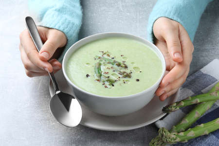 Woman eating delicious asparagus soup at light gray table, closeupの写真素材