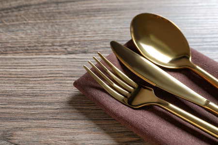 Set of golden cutlery with napkin on wooden table, closeup. Space for textの写真素材