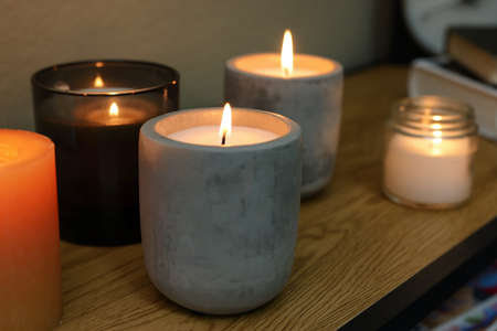 Lit candles in different holders on wooden table indoorsの写真素材