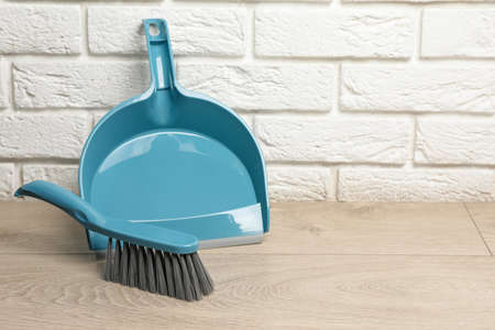 Plastic whisk broom with dustpan near white brick wall indoors. Space for textの写真素材