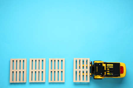 Toy forklift and wooden pallets on light blue background, flat lay. Space for textの写真素材