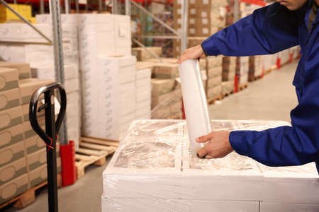 Worker wrapping boxes in stretch film at warehouse, closeupの写真素材