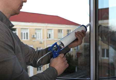 Construction worker sealing window with caulk indoors, closeup