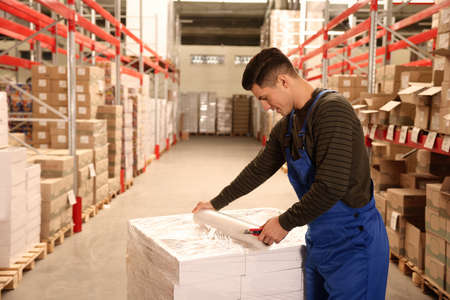 Worker wrapping boxes in stretch film at warehouseの写真素材