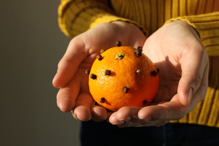 Woman holding pomander ball made of tangerine with cloves on gray background, closeupの写真素材