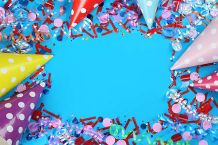 Frame of colorful serpentine streamers, party hats and confetti on light blue background, flat lay....