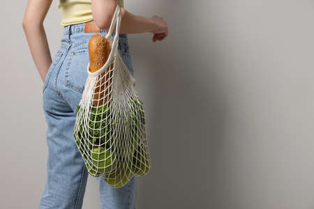 Woman with eco bag full of products on light background, closeup. Space for textの写真素材