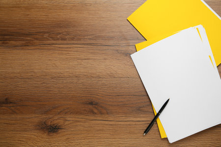 Yellow files with blank sheets of paper and pen on wooden table, flat lay. Space for text