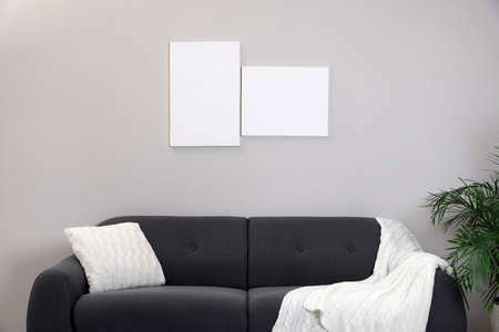 Blank canvas on wall over comfortable sofa indoors. space for designの写真素材