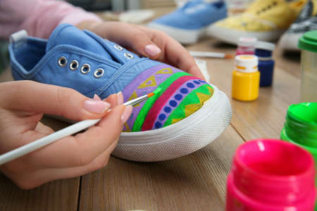 Woman painting on sneaker at wooden table, closeup. custom shoes