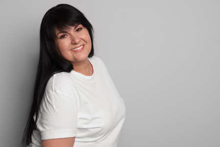 Beautiful overweight mature woman with charming smile on light gray background. Space for text