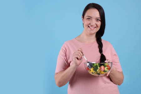 Beautiful overweight woman eating salad on light blue background, space for text. healthy diet