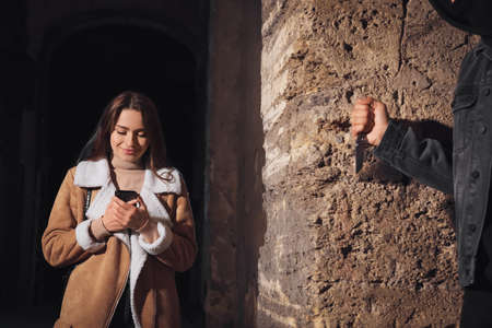 Criminal with knife hiding behind wall and waiting for victim near alley at night