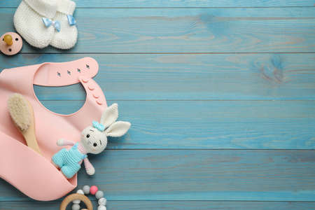 Flat lay composition with silicone baby bib, toys and accessories on light blue wooden background....