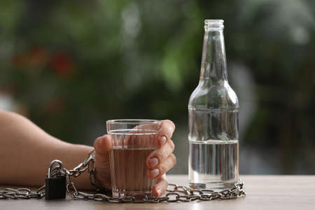 Man chained to glass of vodka at table against blurred background, closeup. alcohol addiction