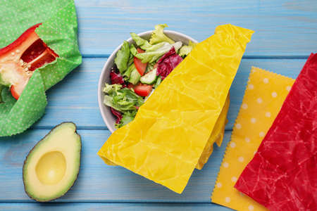 Different products in beeswax food wraps on light blue wooden table, flat layの写真素材