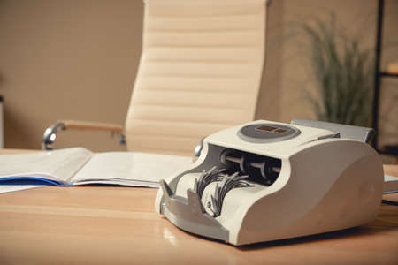 Modern banknote counter on wooden table indoors. Space for textの写真素材
