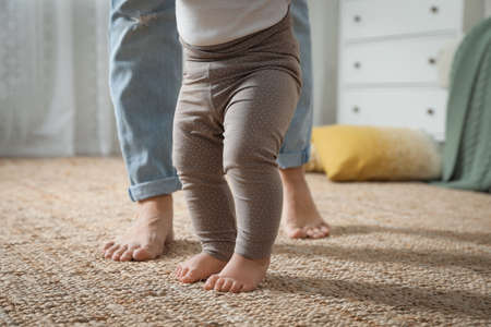 Mother supporting her baby daughter while she learning to walk at home, closeupの写真素材