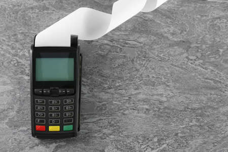 New modern payment terminal with blank paper bill on gray table, top view. Space for text