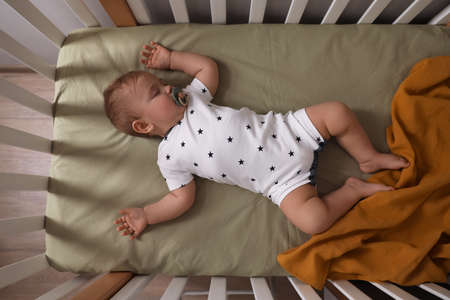Adorable little baby with pacifier sleeping in crib indoors, top view