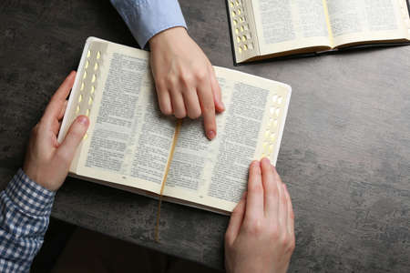 Humble couple reading Bibles at gray table together, top view