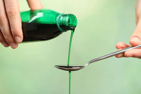 Woman pouring cough syrup into spoon on light green background, closeupの写真素材