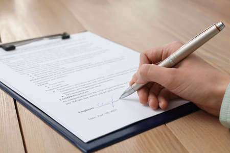 Woman signing contract at wooden table, closeup.の写真素材