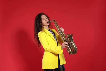 Beautiful African American woman playing saxophone on red backgroundの写真素材