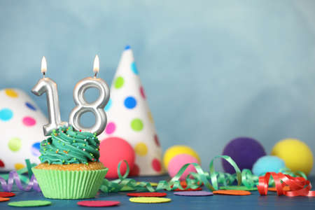 18th birthday, coming of age party. Delicious cupcake with number shaped candles on blue table,...