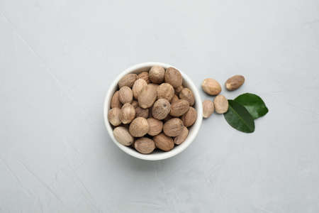Bowl with nutmeg seeds and leaves on light table, flat lay