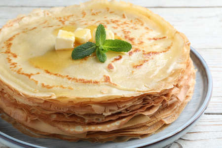 Stack of delicious crepes with mint and melting butter on white wooden table, closeup