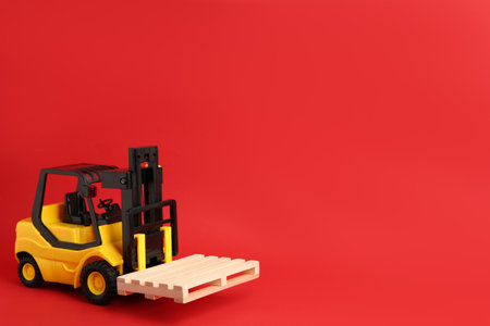 Toy forklift with wooden pallet on red background, space for textの写真素材