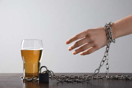 Woman chained to glass of beer at table against white background, closeup. alcohol addiction