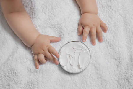 Cute little baby playing with jar of moisturizing cream on towel, closeupの写真素材