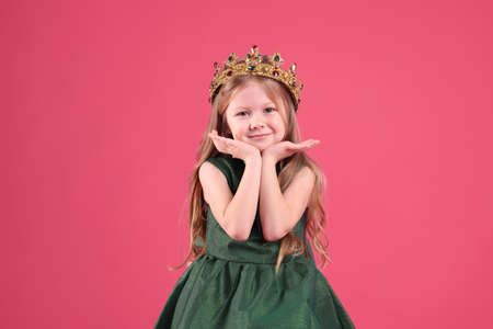 Cute girl in fairy dress and golden crown with gems on pink background. little princessの写真素材