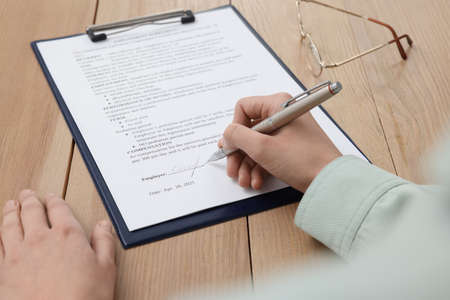 Woman signing contract at wooden table, closeup.の写真素材