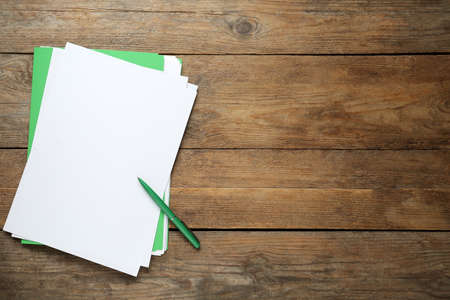 Light green file, blank sheets of paper and pen on wooden table, top view. Space for text