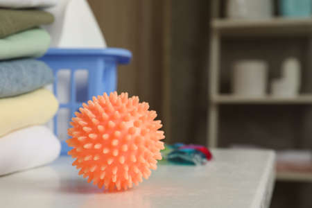 Orange dryer ball on white table near stacked clean towels in laundry room, closeup. Space for textの写真素材