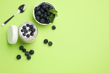Jar of fresh yogurt with blueberry and spoon on light green background, flat lay. Space for textの写真素材