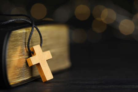 Christian cross and Bible on black wooden table against blurred background, closeup. Space for textの写真素材