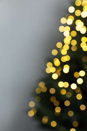 Blurred view of beautiful fir tree with Christmas lights on gray background, space for textの写真素材