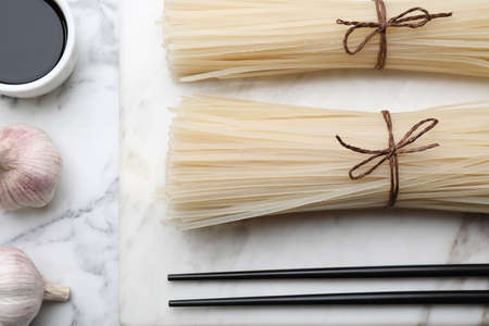 Flat lay composition with uncooked rice noodles, soy sauce and chopsticks on white marble tableの写真素材
